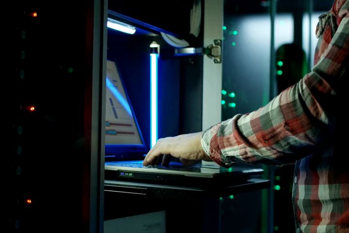 An engineer using a laptop to configure equipment in front of a server cabinet